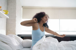 Woman feeling tired and stretching in bed - sleep problems