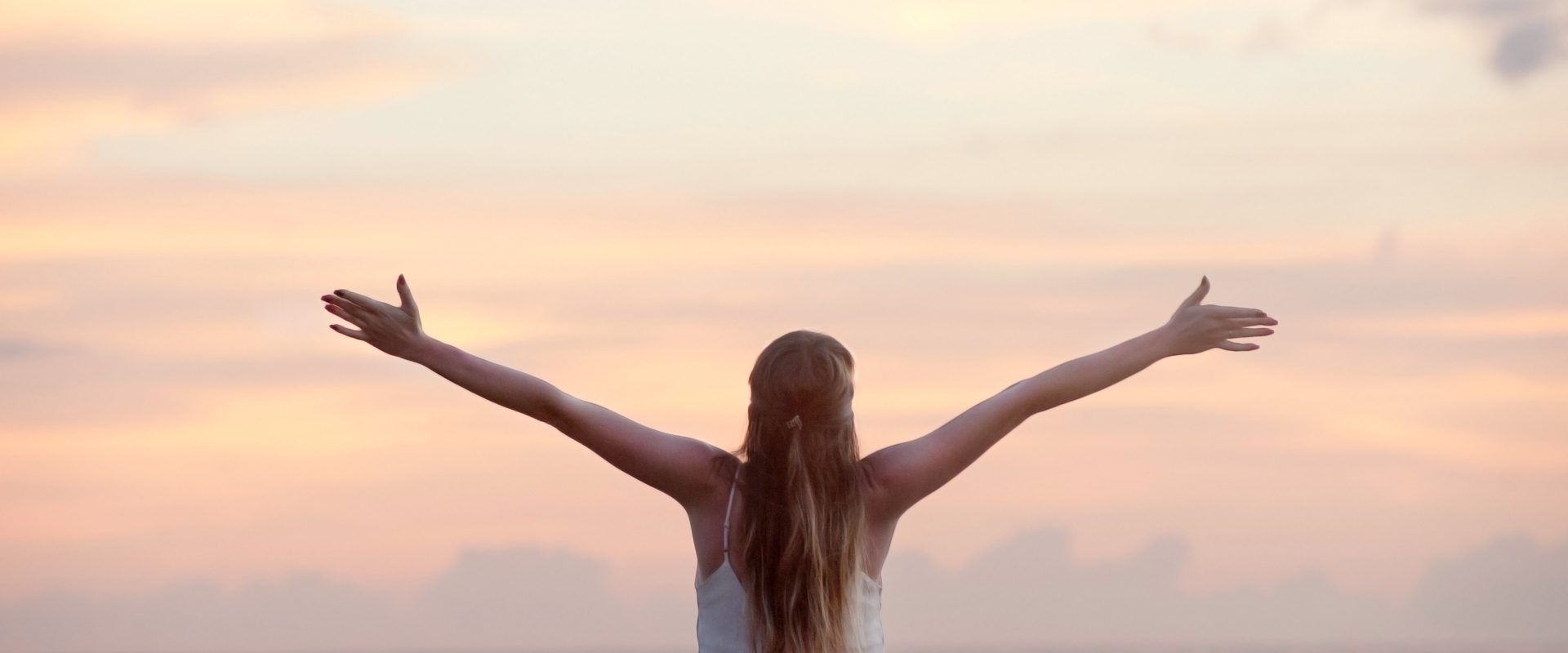 a woman with open arms looking at the ocean