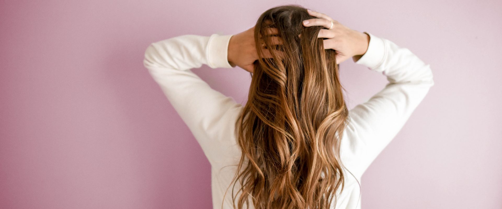 Woman with hands in hair in front of a pink wall